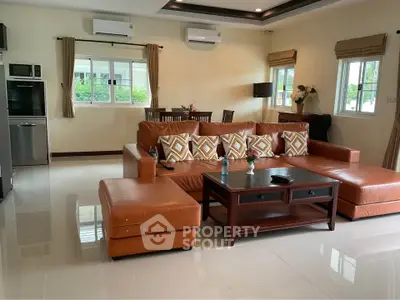 Spacious living room with modern leather sofa and dining area, featuring large windows and air conditioning.