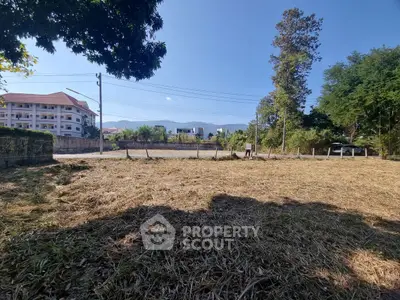 Spacious vacant land with potential for development, surrounded by lush greenery and nearby residential buildings.