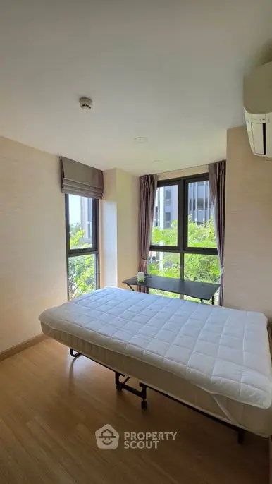 Bright bedroom with large windows and a minimalist design, featuring a comfortable bed and lush green views.