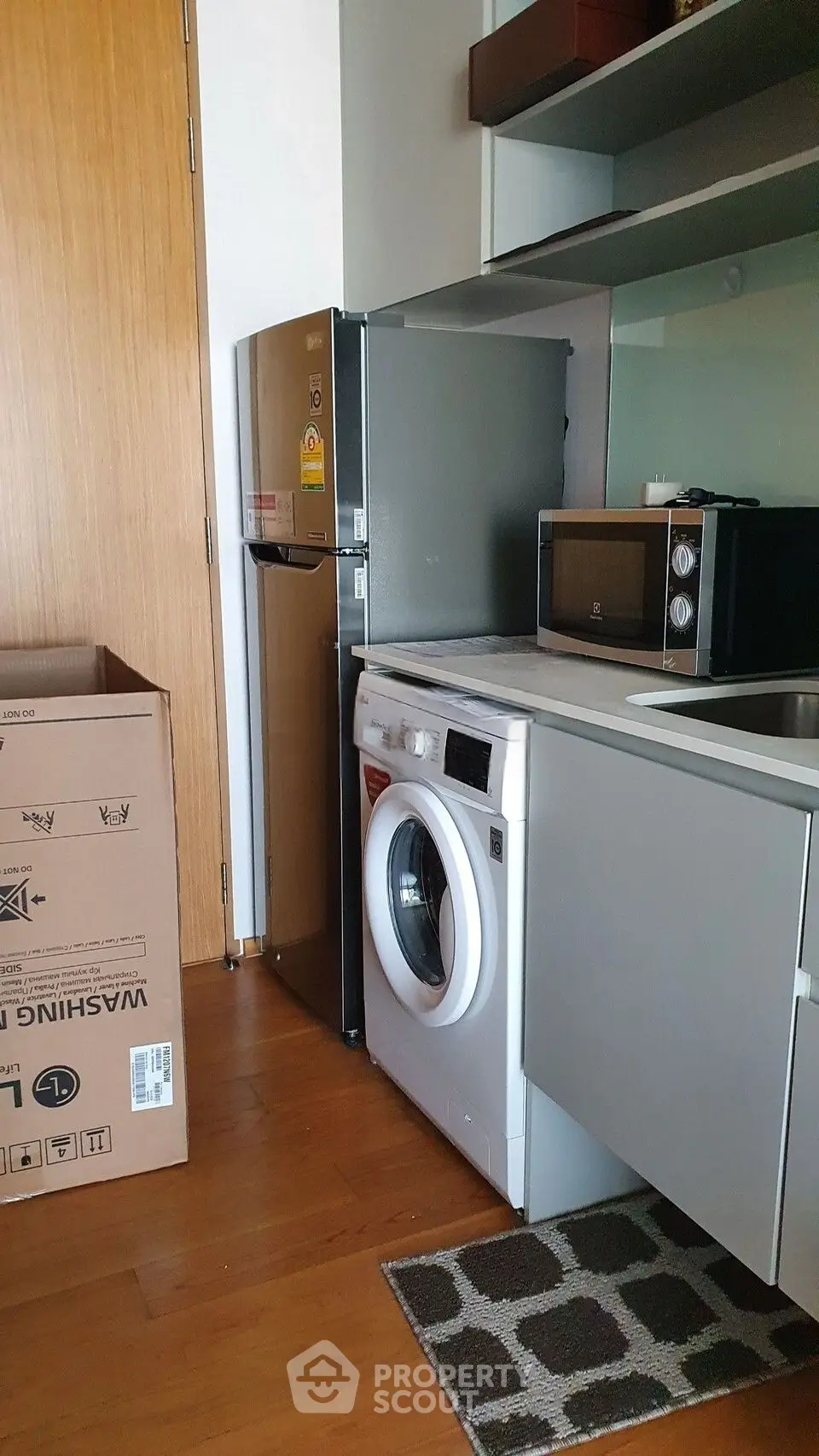 Modern kitchen with washing machine, fridge, and microwave in compact layout.