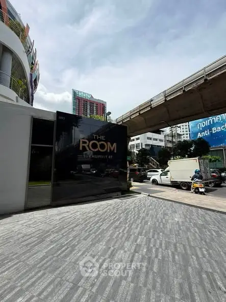 Modern urban building entrance with sleek design near elevated train tracks.