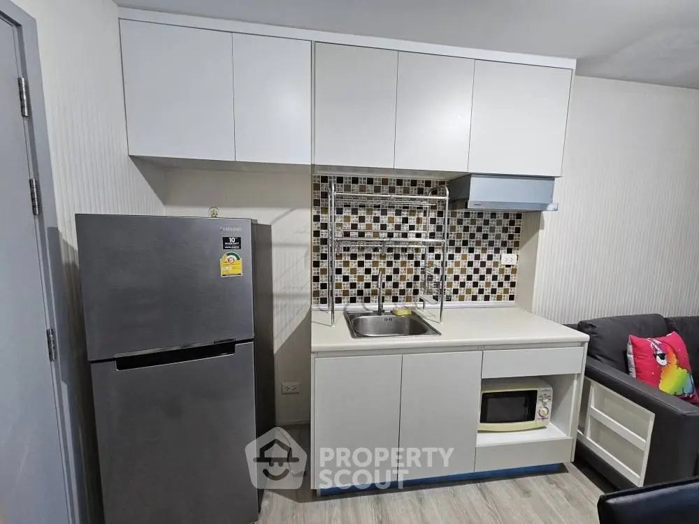 Modern compact kitchen with sleek cabinetry and stainless steel fridge in a cozy apartment.
