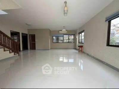 Spacious open-plan living room with large windows and elegant staircase, perfect for modern family living.