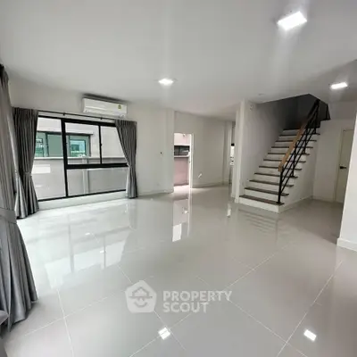 Spacious modern living room with large windows and sleek staircase in a contemporary home.