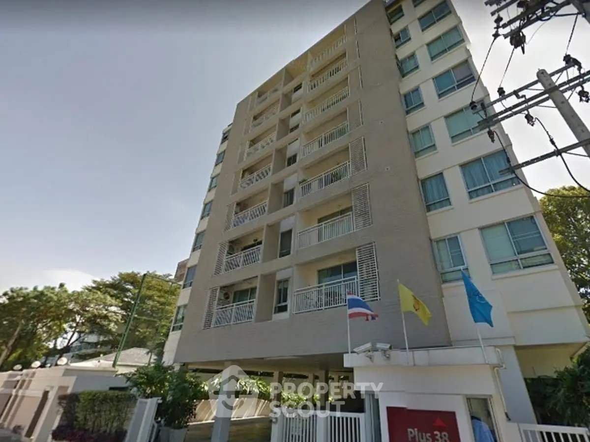 Modern multi-story residential building with flags and lush greenery, ideal urban living.