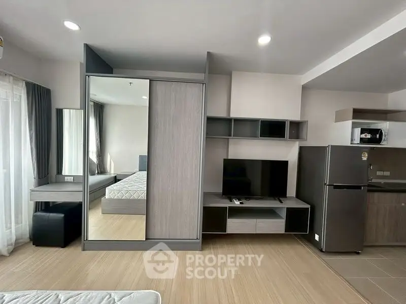Modern studio apartment with sleek furniture and open layout, featuring a cozy bed, TV, and kitchen area.