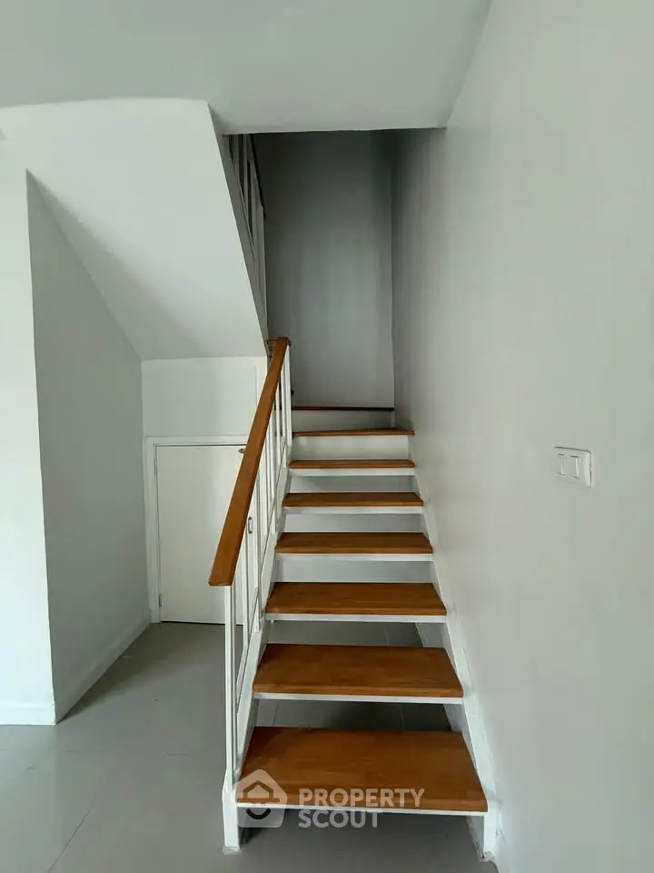 Modern staircase with wooden steps and white railing in a minimalist interior.