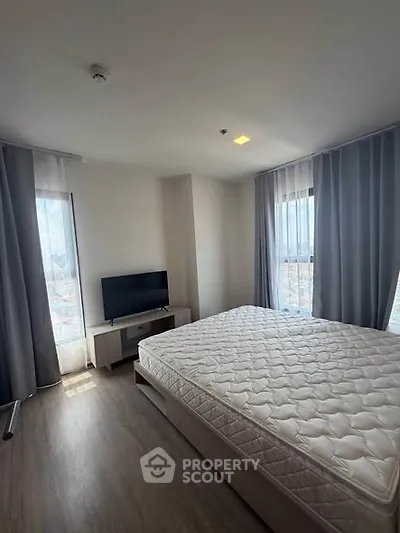 Spacious bedroom with large windows and natural light, featuring a modern bed and flat-screen TV.