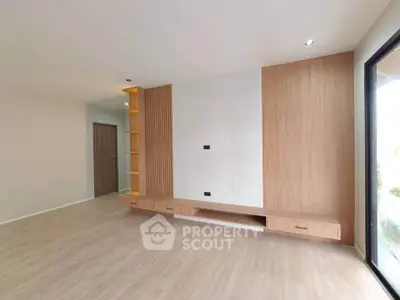 Spacious modern living room with built-in wooden entertainment unit and large window.