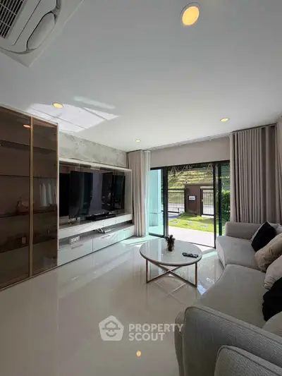 Modern living room with large TV, sleek furniture, and natural light from glass doors.