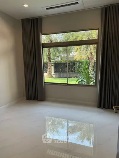 Spacious room with large window offering lush garden view, perfect for serene living.