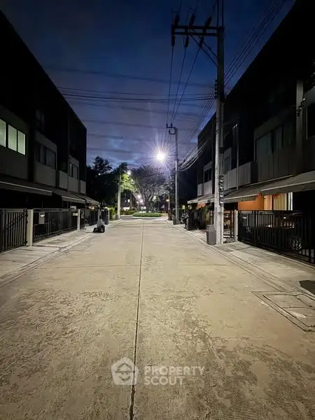 Charming residential street view at dusk with modern townhouses and ambient lighting.
