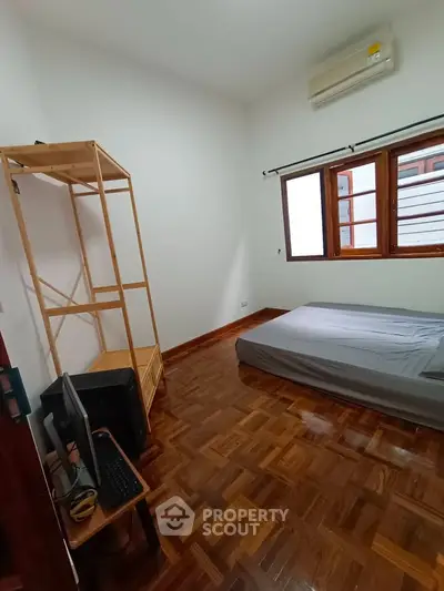 Cozy bedroom with wooden flooring, air conditioning, and natural light from large window.