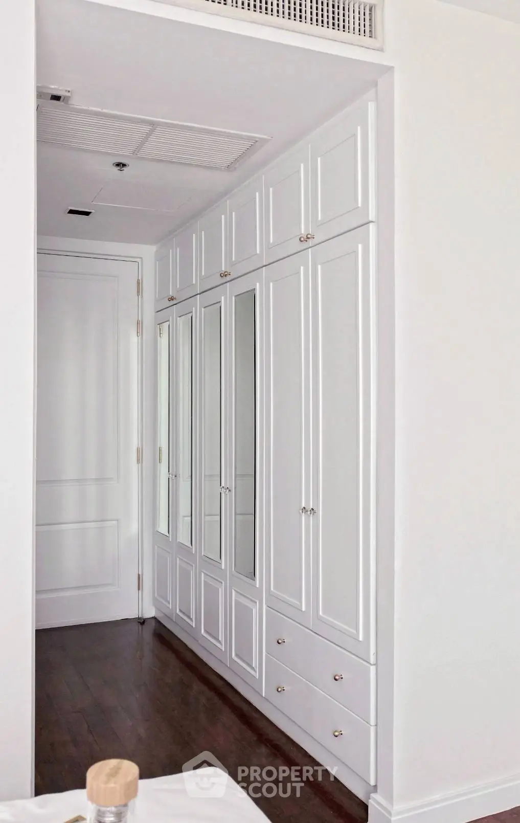 Spacious white built-in wardrobe with mirrored doors in elegant bedroom setting.