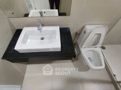 Modern bathroom with sleek sink and toilet design, featuring neutral tile accents.