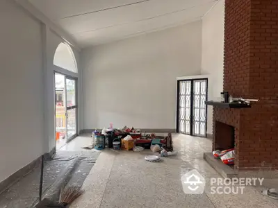 Spacious living room with brick fireplace and large window under renovation