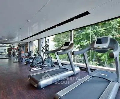 Modern gym with large windows and state-of-the-art equipment in luxury building.