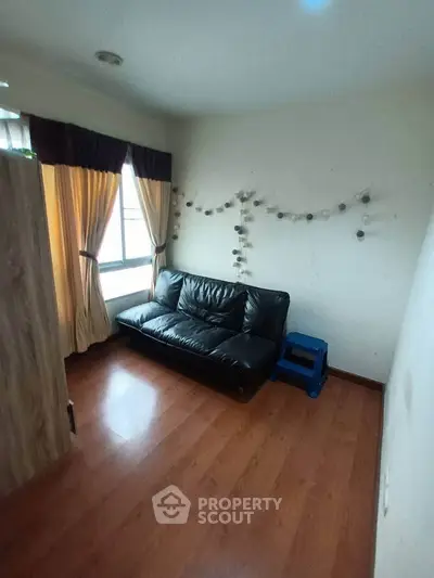 Cozy living room with wooden flooring and stylish black leather sofa, perfect for relaxation.