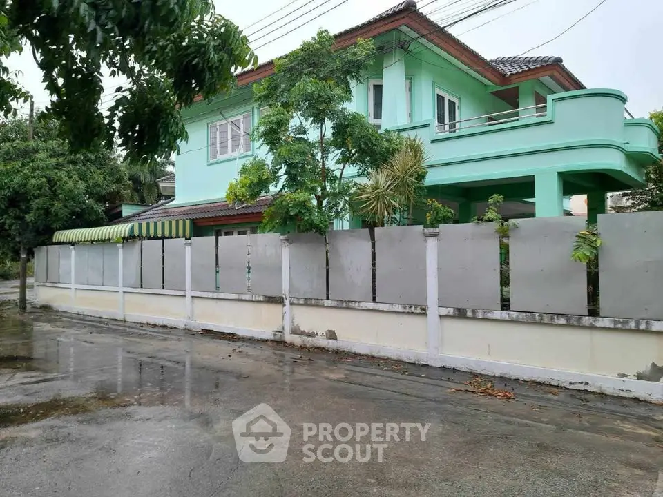 Charming two-story green house with lush garden and privacy fence in serene neighborhood.