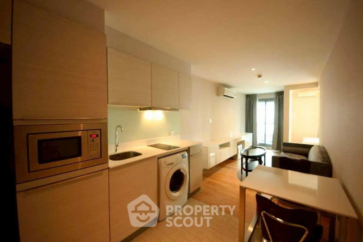 Modern apartment interior with kitchen and living area featuring washing machine and microwave.