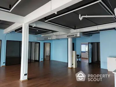 Spacious commercial space with polished wooden floors, blue walls, and exposed ceiling beams, ideal for a bespoke office or studio.