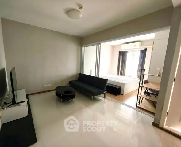 Modern living room with sleek furniture and open layout leading to a cozy bedroom.