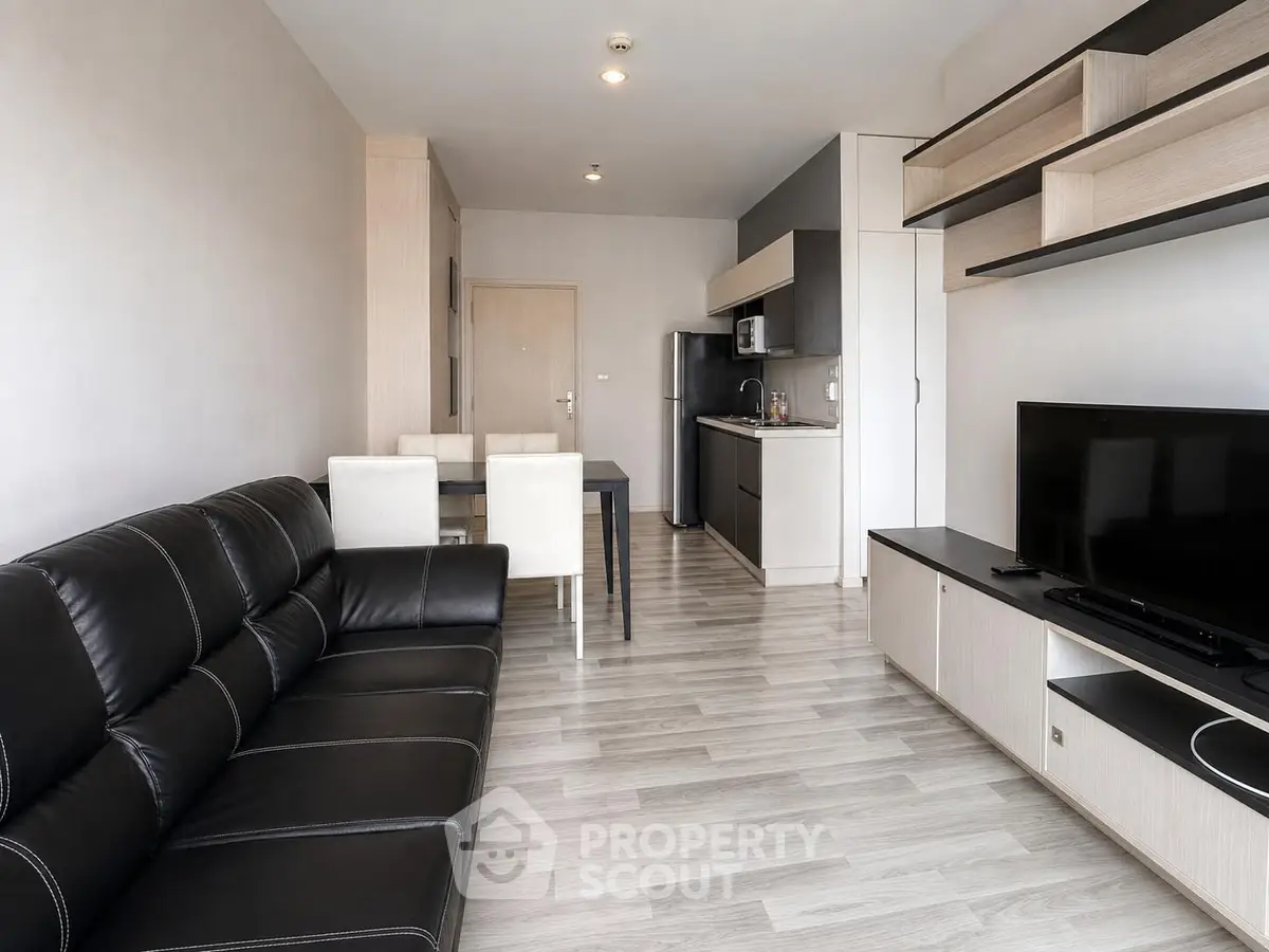 Modern open-plan living room with sleek black leather sofa and integrated kitchen area.