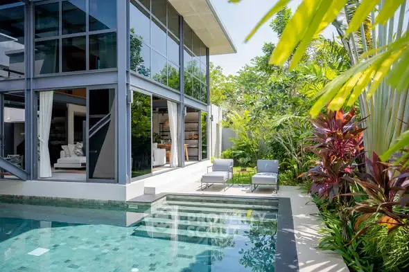 Luxurious modern home with glass facade and inviting pool surrounded by lush greenery.