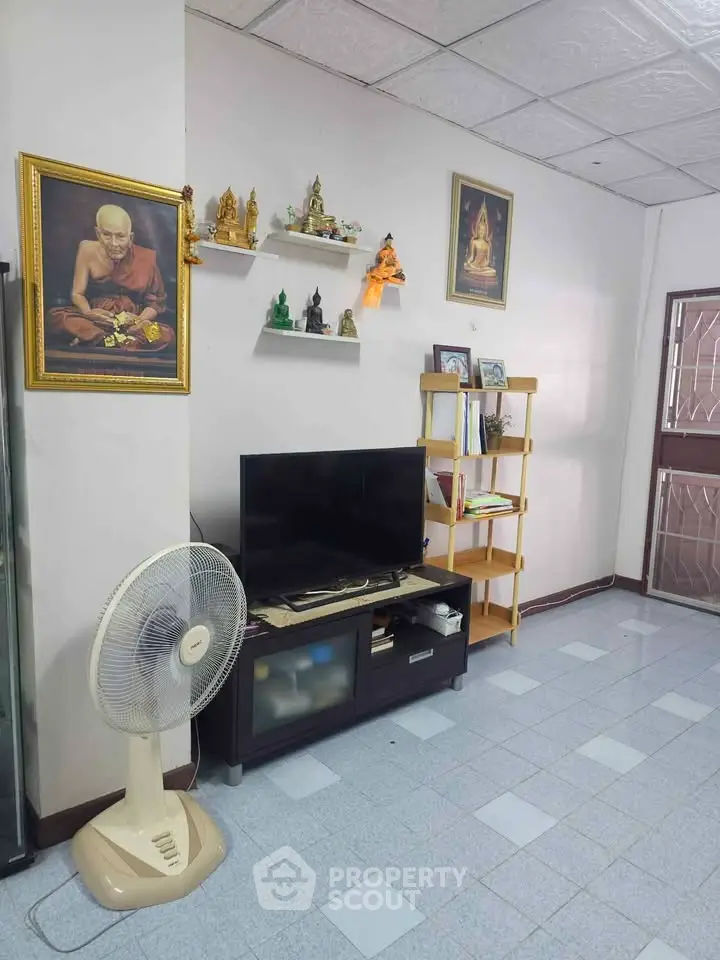 Cozy living room with TV, fan, and spiritual decor, perfect for relaxation and meditation.
