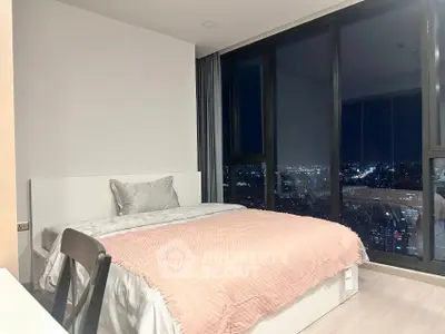 Modern bedroom with stunning city view through floor-to-ceiling windows at night.
