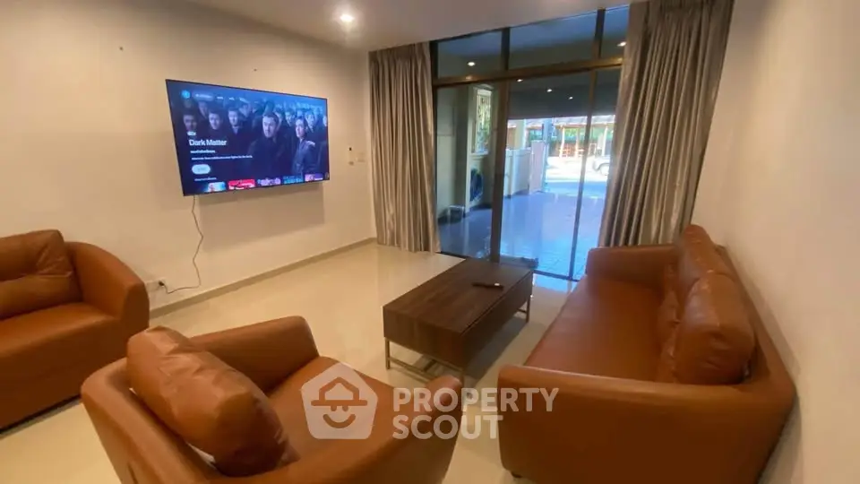Spacious living room with modern leather sofas and large TV, featuring a view of the outdoor patio.
