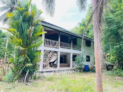 Charming two-story house surrounded by lush greenery, featuring a spacious balcony and rustic staircase.