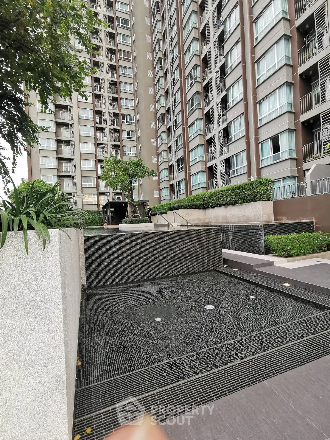 Modern residential building exterior with landscaped garden and water feature.