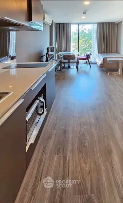 Modern open-layout living room with kitchen, featuring sleek design and large window with natural light.