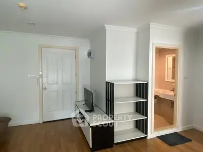 Modern apartment interior with wooden flooring, TV unit, and open bathroom entrance.