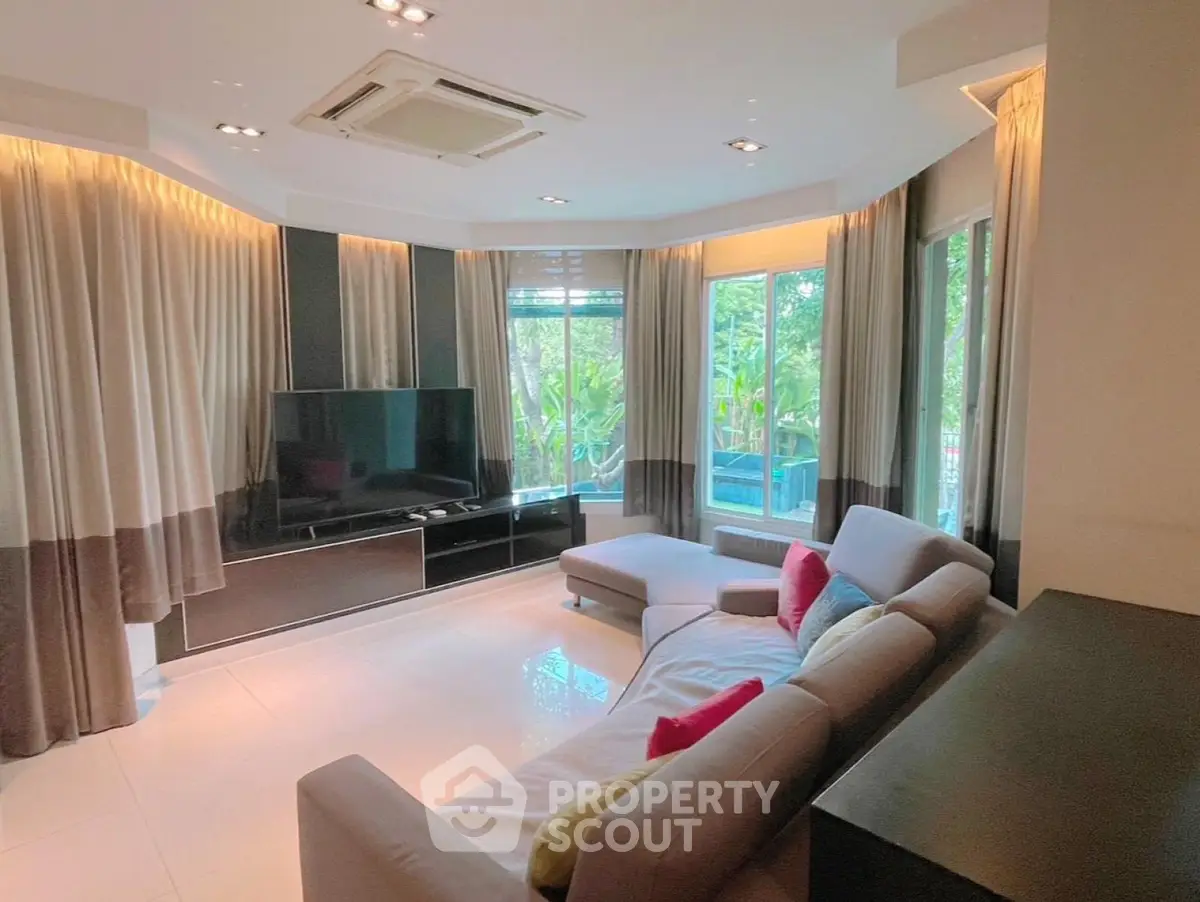 Spacious living room with modern decor and large windows offering lush garden views.