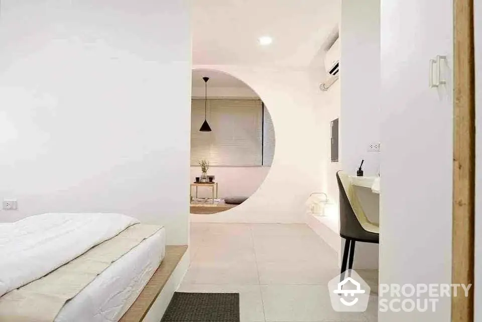 Modern minimalist bedroom with unique circular wall opening and sleek furnishings.