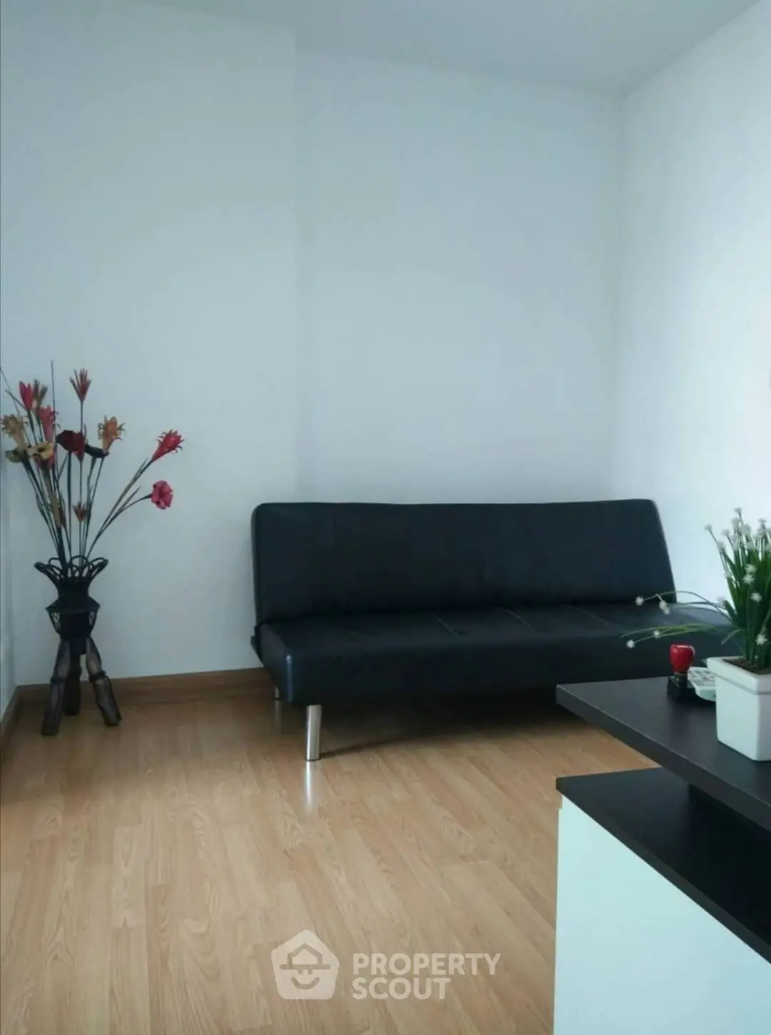 Modern minimalist living room with sleek black sofa and wooden flooring.
