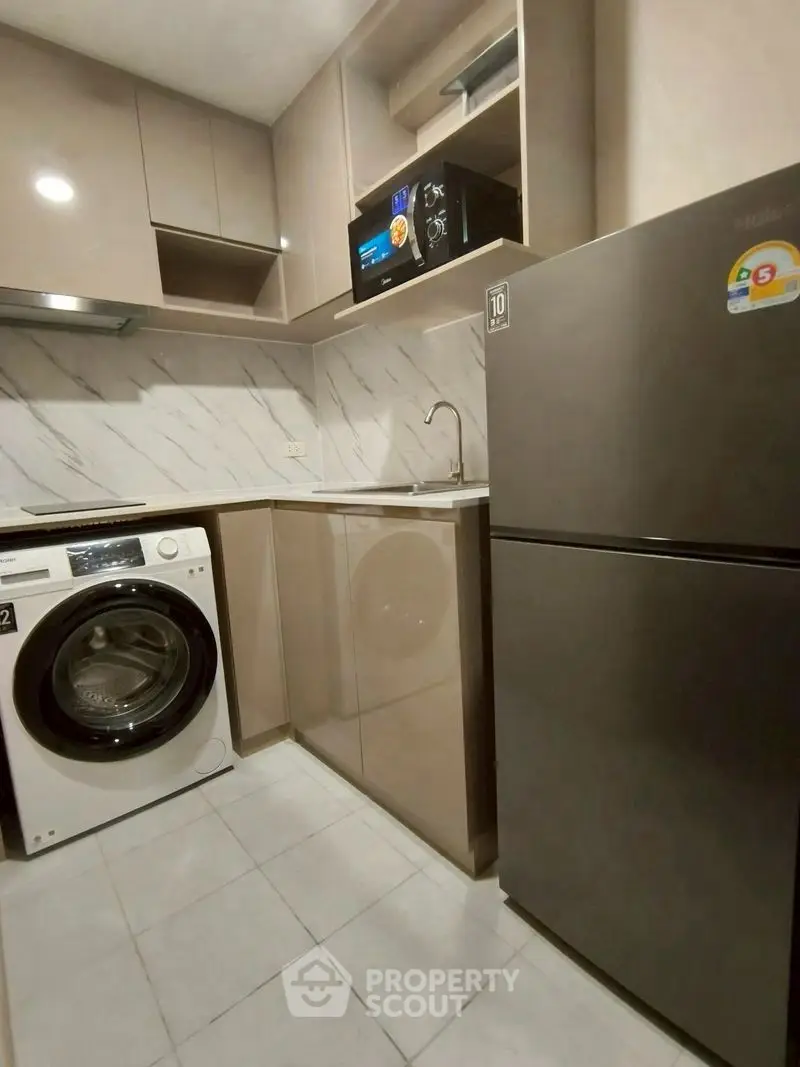 Modern kitchen with sleek appliances and marble backsplash in compact layout.