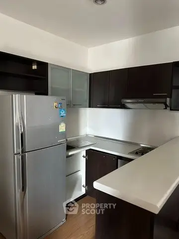 Modern kitchen with sleek dark cabinets and stainless steel fridge in a compact layout.