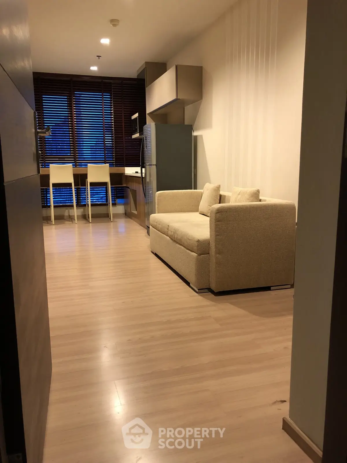 Modern open-plan living room with cozy sofa and dining area, featuring sleek wooden flooring and ambient lighting.