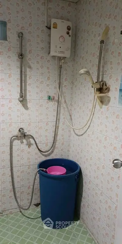 Compact bathroom with water heater and bucket, tiled walls and floor, practical setup for efficient use.