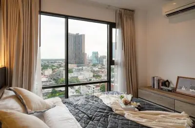 Modern bedroom with city view from large window, cozy bedding and stylish decor.