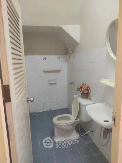 Cozy bathroom with sloped ceiling and simple decor, featuring a toilet, sink, and floral arrangement.