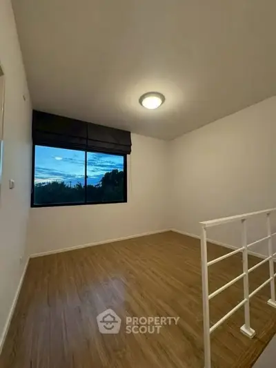 Spacious room with wooden flooring and large window offering scenic views, perfect for a cozy living space.