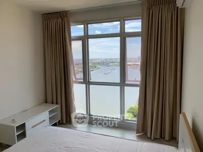 Bright bedroom with stunning river view through large windows, ideal for relaxation.