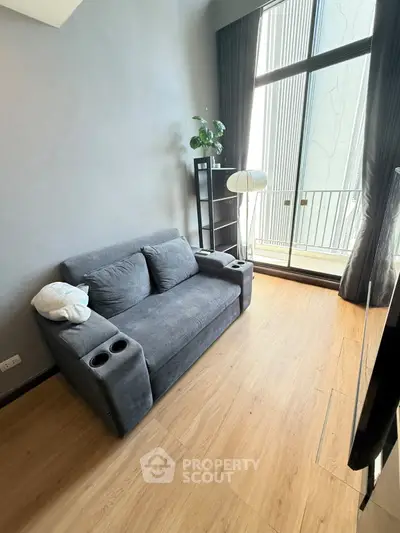 Modern living room with cozy gray sofa and floor-to-ceiling windows leading to a small balcony.