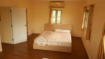 Spacious bedroom with wooden flooring and natural light