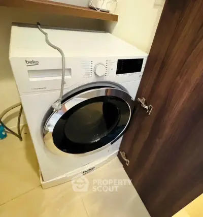 Modern washing machine in a compact laundry space with wooden cabinet door.