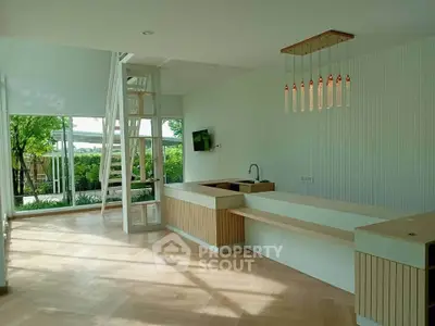 Spacious modern living room with open kitchen and stylish lighting, featuring large windows and garden view.